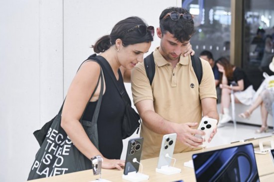 2025年7月17日，两名西班牙游客在位于上海市南京路步行街的华为商店里浏览手机产品。（图片来源：新华社）